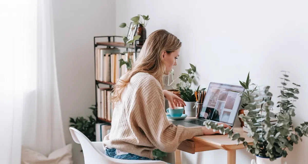 Blogger working at a bright desk with laptop, plants, and books