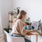 Blogger working at a bright desk with laptop, plants, and books