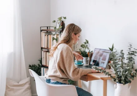Blogger working at a bright desk with laptop, plants, and books
