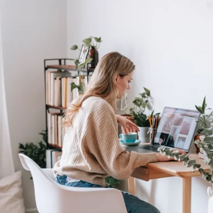 Blogger working at a bright desk with laptop, plants, and books
