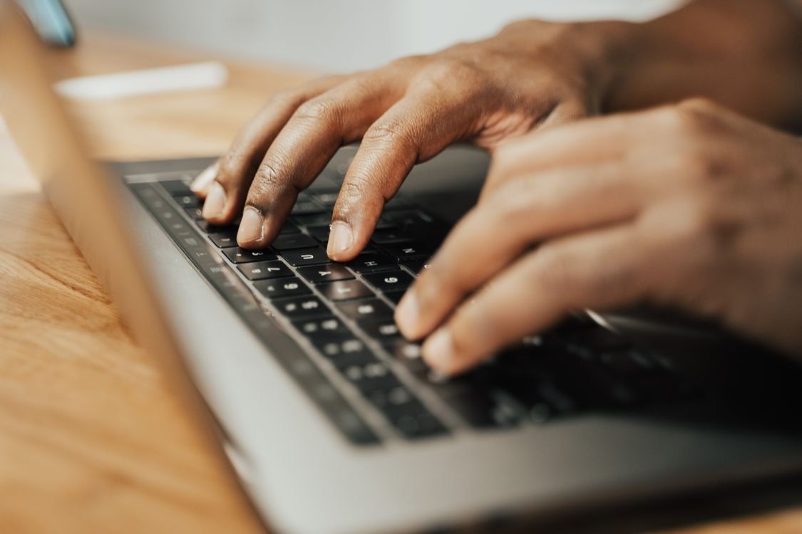 Close-up of a person using a laptop on a wooden desk