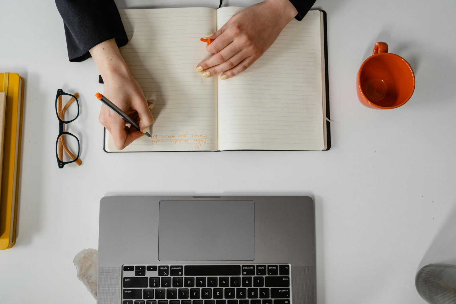 Overhead view of a notebook, laptop, glasses and coffee on a writing desk